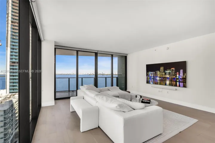 Floor-to-ceiling glass windows, wide-plank wood-finish flooring, metal-framed balcony access, and expansive water scenery