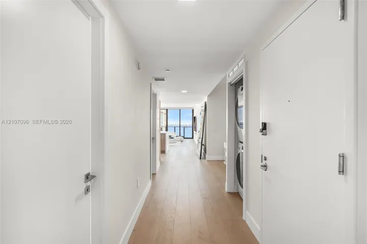Hallway featuring light-tone wood-finish flooring, recessed lighting, and a built-in stacked laundry unit