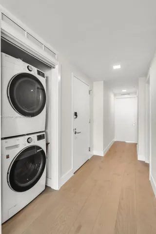Stacked white front-load laundry appliances, light-toned wood-finish flooring, recessed ceiling lighting, and solid core doors