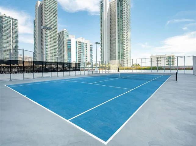Rooftop tennis court featuring a hard surface, integrated net, perimeter fencing, and stadium-style lighting