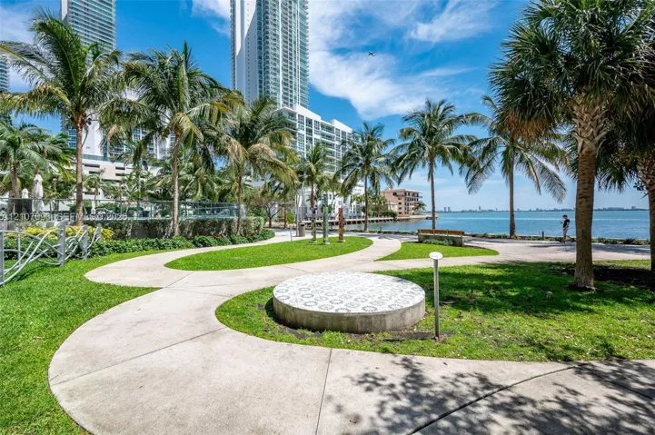 Waterfront grounds featuring mature palm trees, curated green space, concrete pathways, and an ornamental tiled pedestal
