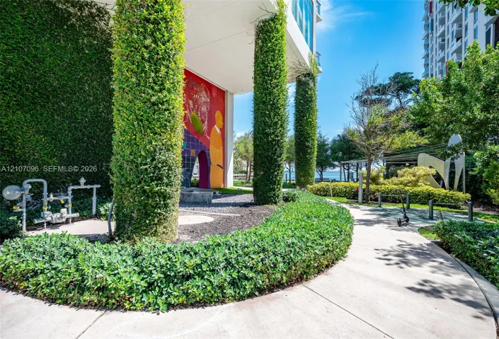 Landscaped grounds featuring ivy-covered structural columns, decorative exterior mural, paved walkways, and manicured shrubbery