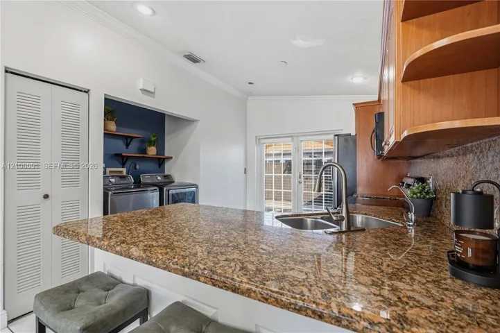 Kitchen featuring a stone-surface breakfast bar, wood cabinetry, recessed lighting, and a dedicated laundry area with built-in shelving