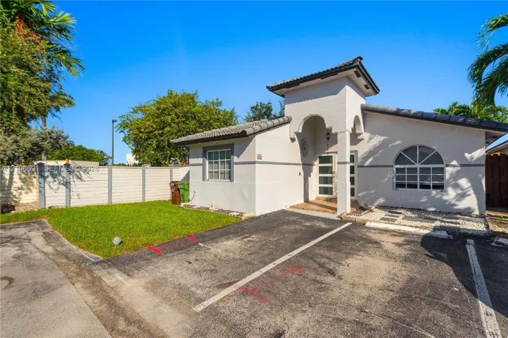 Stucco exterior featuring a covered entryway, arched window details, a tiled roof, and a private green space