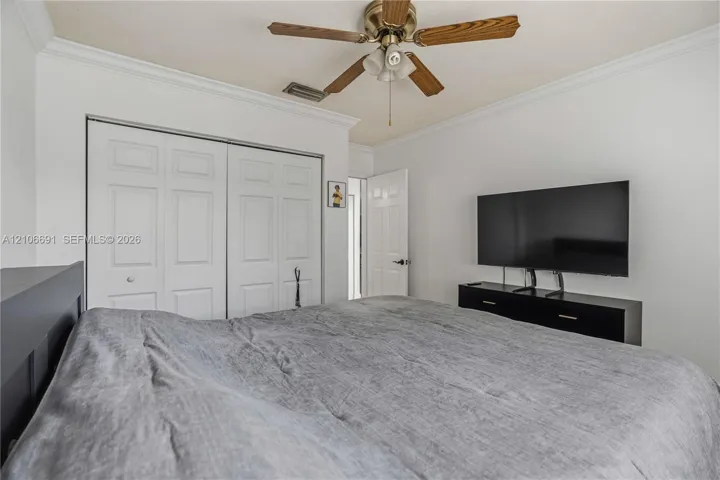 Neutral wall color palette, white bi-fold closet doors, crown molding, and a multi-blade ceiling fan with integrated light fixture