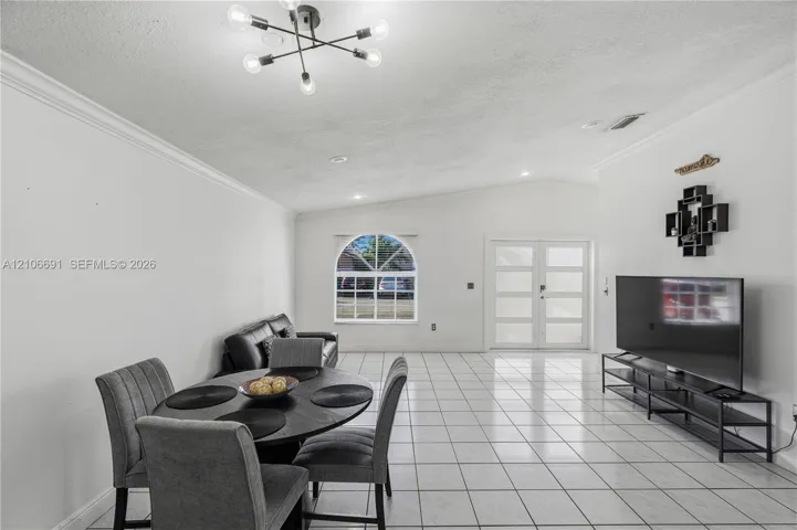 Living area featuring vaulted ceilings, ceramic tile flooring, arched window, and six-light modern chandelier