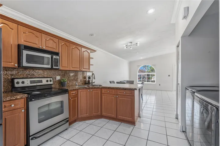Kitchen featuring medium-tone wood cabinetry, stone countertops, stainless steel appliances, tile flooring, and a multi-light ceiling fixture