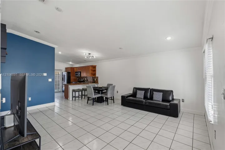 Open-concept interior featuring large-format tile flooring, crown molding, recessed lighting, and a kitchen with wood-finish cabinetry and a peninsula counter