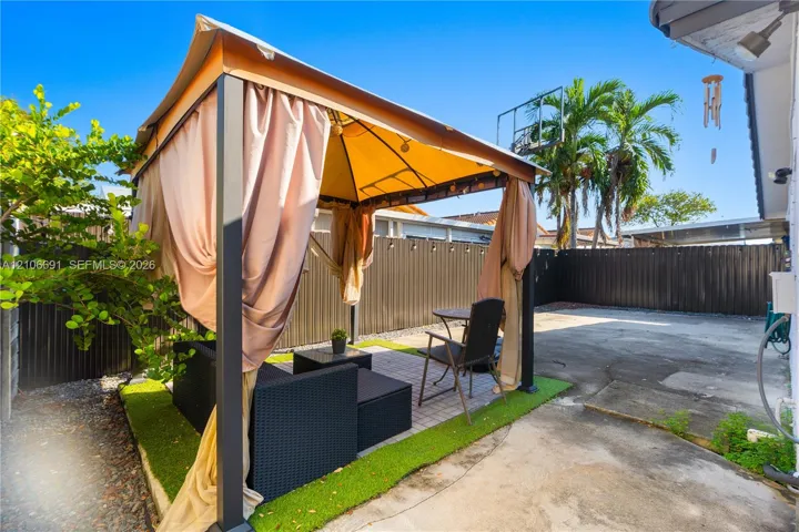 Outdoor space featuring a permanent metal-framed gazebo, concrete patio, privacy fencing, and turf border