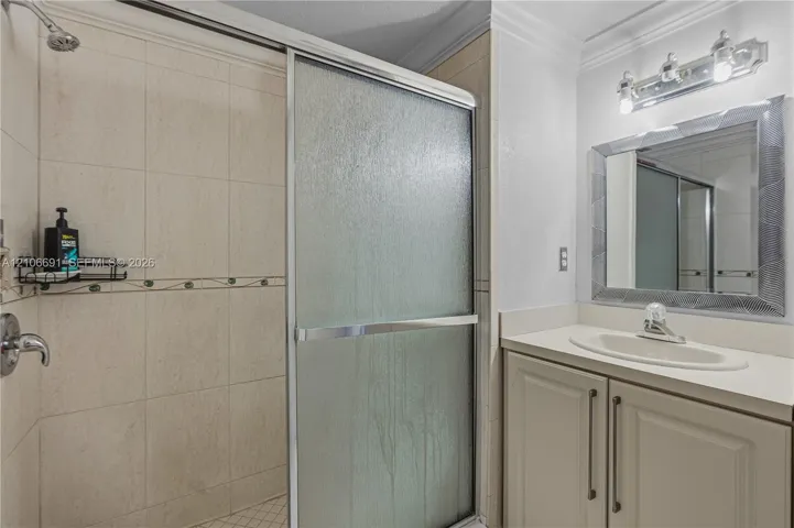Bathroom featuring a vanity with integrated sink, chrome faucet, wall-mounted vanity lighting, mirror with a decorative frame, and a tiled shower enclosure with sliding glass doors