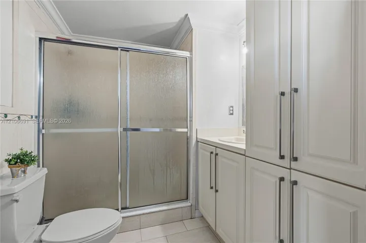 Bathroom featuring a glass-enclosed shower, expansive floor-to-ceiling cabinetry, neutral tile flooring, and integrated countertop vanity