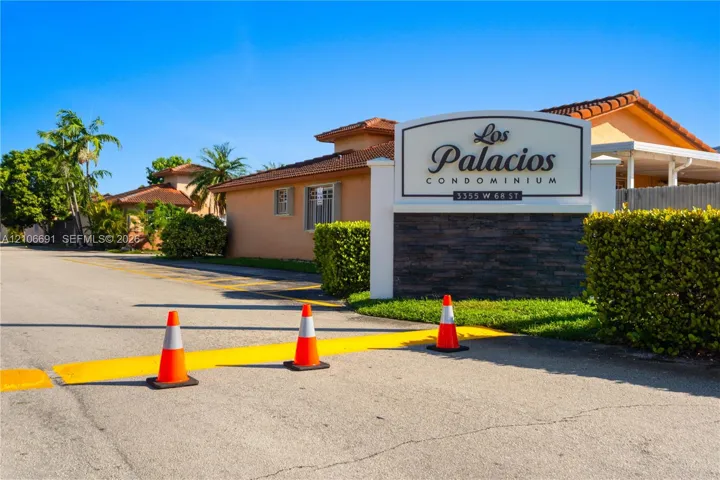 Los Palacios Condominium entrance featuring stucco-finished building exteriors, tile roofing, and a decorative stacked-stone monument sign