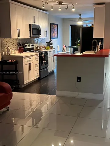 Kitchen featuring white cabinetry with matte black hardware, tiled backsplash, solid surface countertops, and dark floor tiling