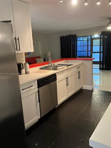 Kitchen featuring white shaker-style cabinetry, stainless steel appliances, a dual-basin sink with a gooseneck faucet, a mosaic tile backsplash, and dark tile flooring