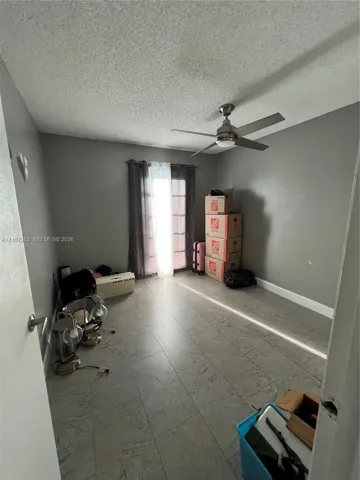 Neutral-toned interior room featuring large-format tile flooring, a brushed metal ceiling fan, and sliding glass doors