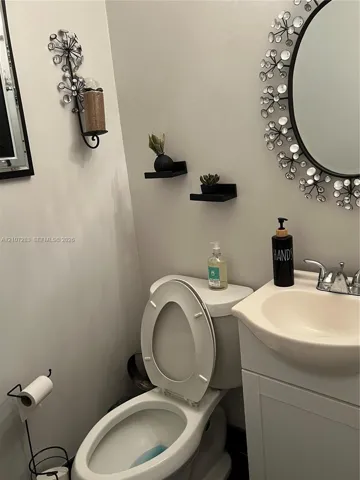 Vanity featuring a molded-top sink with metallic-finish faucet, accompanied by two wall-mounted floating shelves and a circular wall mirror with decorative surround