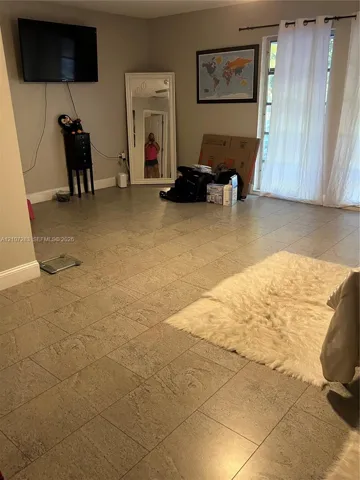 Living area featuring neutral-toned tile flooring and glass paneled doors with a curtain rod fixture