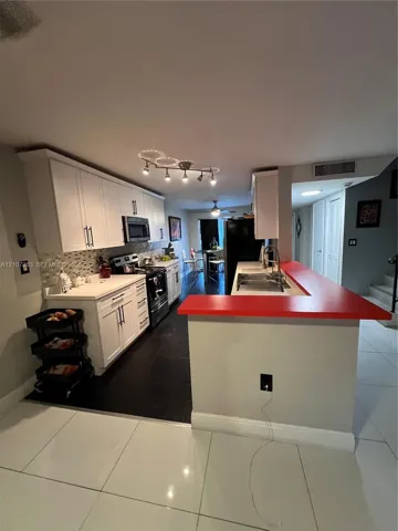 Kitchen featuring white shaker-style cabinetry, a contrasting red peninsula countertop, dark tile flooring, a multi-bulb track lighting fixture, and a tile backsplash