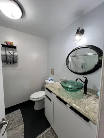 Stone countertop with a glass vessel sink, matte black faucet, oval wall mirror, and dark tile flooring
