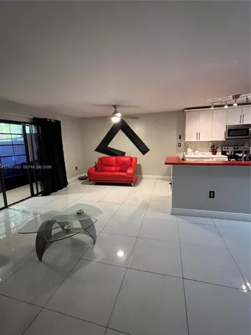 Large format tile flooring, white cabinetry, integrated peninsula with red countertop, and sliding glass door with dark frame