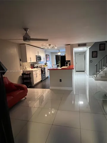 Large-format tile flooring, white cabinetry, integrated kitchen peninsula, ceiling fans, and staircase with iron railing