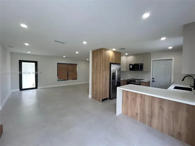 Kitchen featuring a quartz countertop peninsula, stainless steel appliances, matte black fixtures, and light-toned tile flooring