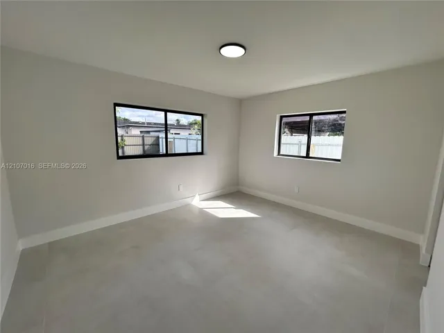 Neutral interior space featuring large-format tile flooring, dual-pane windows with black frames, and a flush-mount LED ceiling light