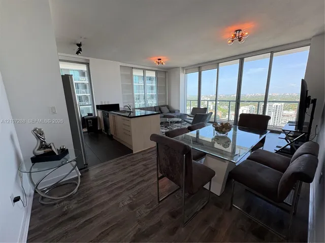 Open-concept interior featuring floor-to-ceiling glass windows, wood-finish flooring, kitchen cabinetry with stone countertops, and dark tile flooring in the cooking area