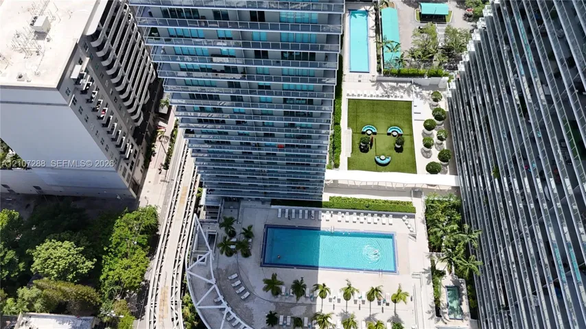 High-rise condominium complex featuring a rectangular swimming pool, lap pool, expansive green space, and landscaped grounds
