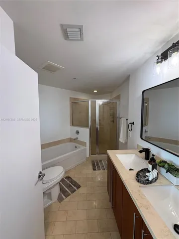 Double vanity with stone-surfaced countertop, dual under-mount sinks, rectangular mirror with black frame, separate glass-enclosed shower, and built-in soaking tub