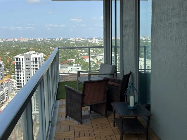 Covered private balcony with modular decking, glass panel railing, and expansive urban scenery
