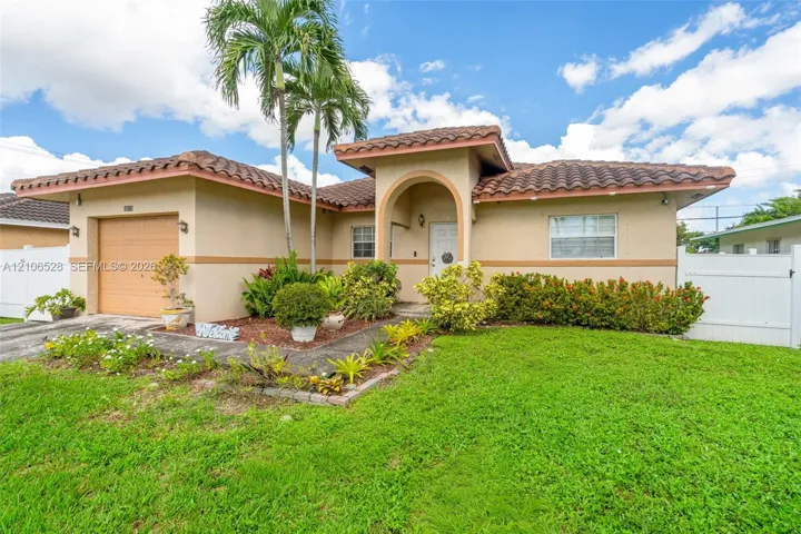 Stucco exterior featuring a terracotta tile roof, arched entryway, single-car garage, and white vinyl privacy fencing