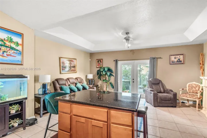 Tray ceiling with recessed lighting, center island with dark stone countertop and wood cabinetry, and double glass doors