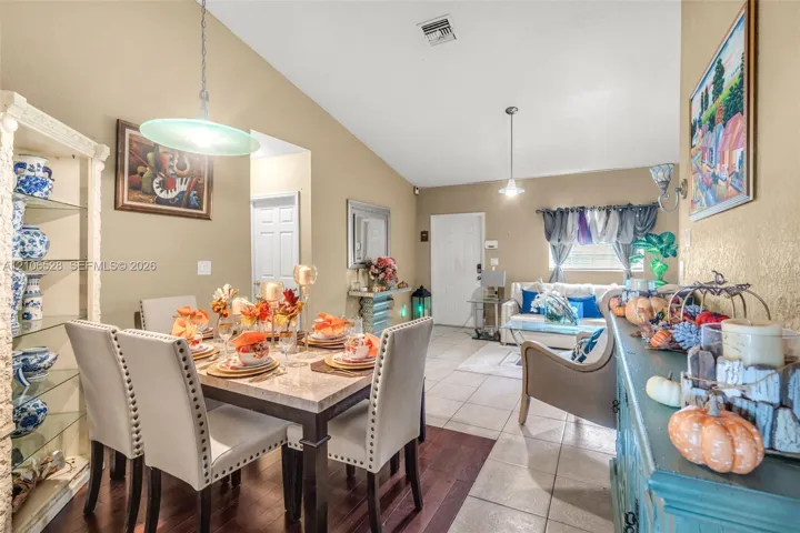 Vaulted ceilings, built-in display shelving, neutral paint palette, pendant lighting, and mixed flooring featuring both ceramic tile and dark wood-finish surfaces