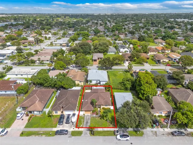 Aerial perspective of a residential property featuring a pitched shingle roof, paved driveway, integrated garage, and mature landscaping