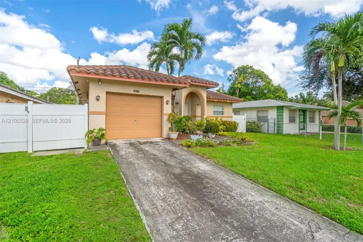 Single-story exterior featuring a clay tile roof, concrete driveway, attached garage, and white vinyl privacy fencing