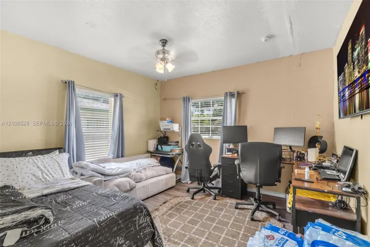Room featuring dual-aspect windows, wood-finish flooring, and a central ceiling fan with integrated lighting