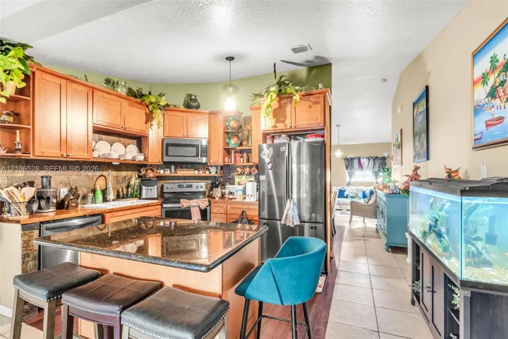 Kitchen featuring wood cabinetry, a stone-surfaced island, a tiled backsplash, and stainless steel appliances