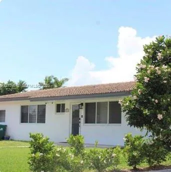 Single-story exterior featuring white stucco siding, a tiled roof, multi-pane windows, and a landscaped front lawn with flowering shrubs