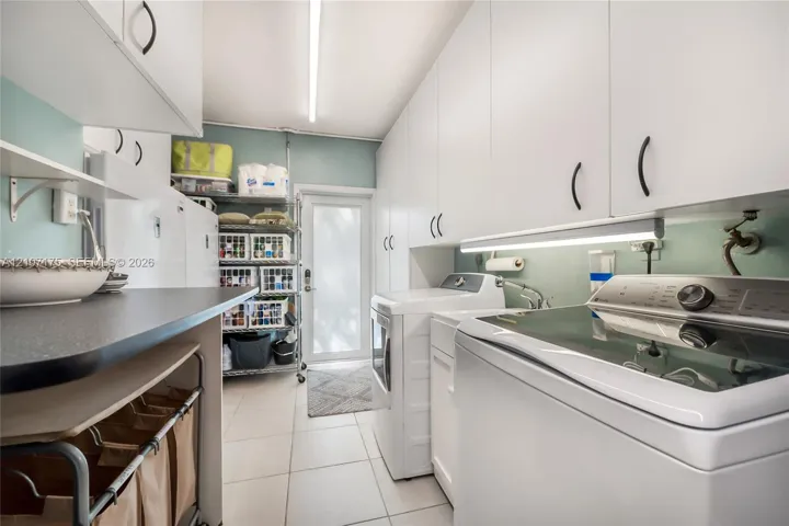 Laundry room featuring laundry tub, extensive white cabinetry, light-toned tile flooring, under-cabinet lighting, and impact glass exterior door.