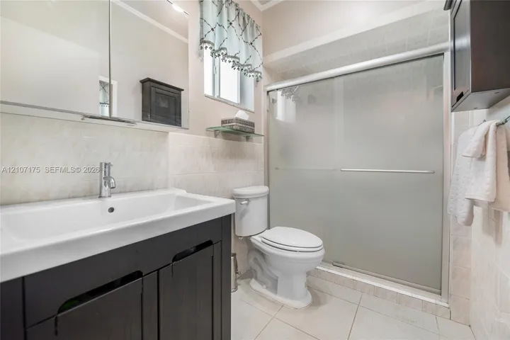 4th Bedroom En-Suite Bath. Dark wood-finish vanity with a rectangular sink, polished chrome faucet, tile-surround shower with frosted sliding glass doors.