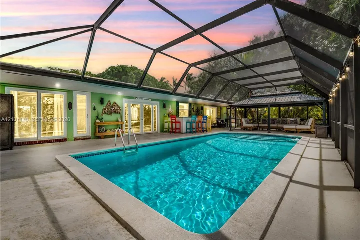 Screen-enclosed swimming pool featuring a concrete deck, built-in bar area, and hardtop pavilion.