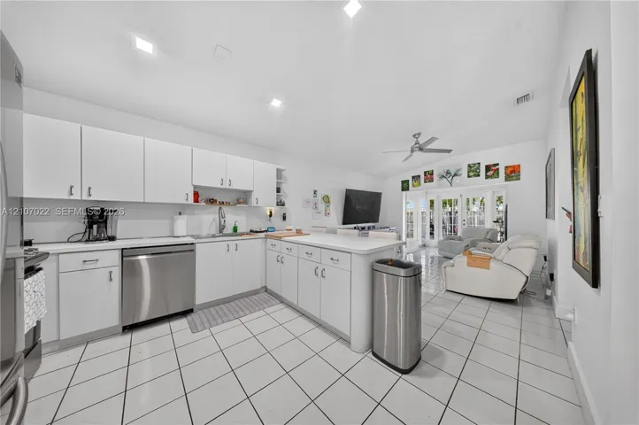 white cabinetry, a central island, recessed lighting, stainless steel dishwasher, and tile flooring, adjoining family room