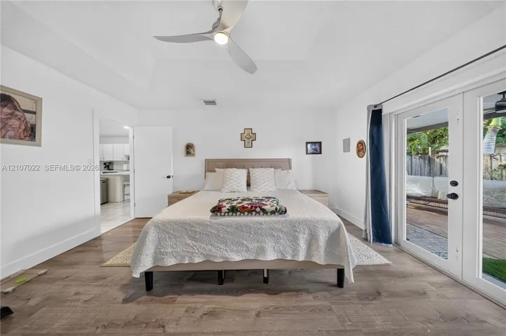 Tray ceiling with a multi-blade ceiling fan, wood-finish flooring, and double glass-paned doors providing exterior access