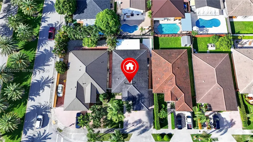 Aerial perspective of a residential property featuring a dark-tiled hip roof, concrete driveway, and mature landscaping