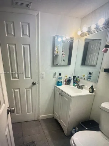Bathroom featuring a vanity with integrated sink, chrome hardware, a wall-mounted mirror, and tile flooring