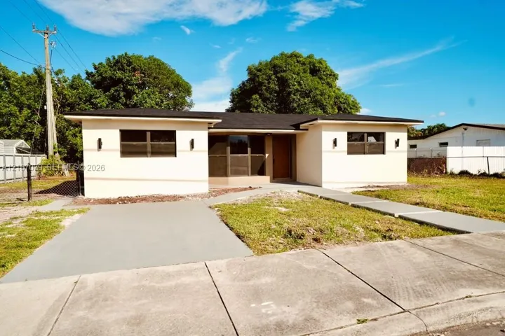Single-story exterior featuring a light-toned smooth finish, horizontal window configuration, dark shingled roof, concrete driveway, and a paved walkway
