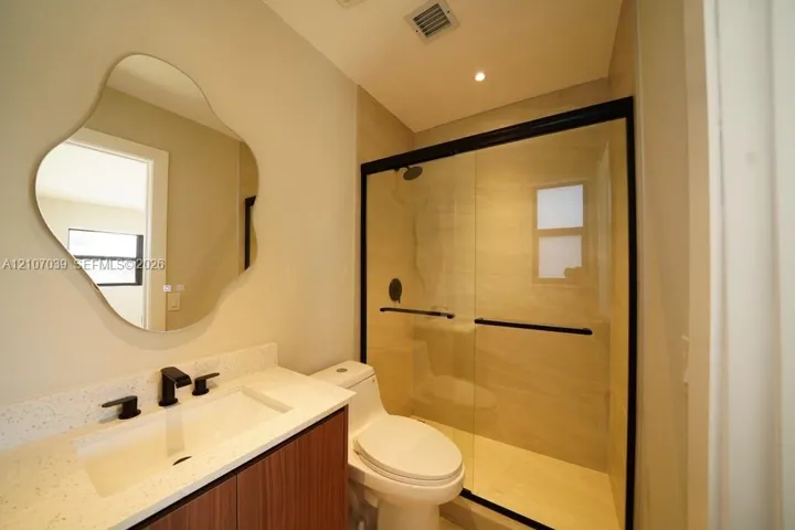 Floating vanity with a light-toned stone countertop, uniquely shaped wall-mounted mirror, matte black plumbing fixtures, and walk-in shower with a glass enclosure