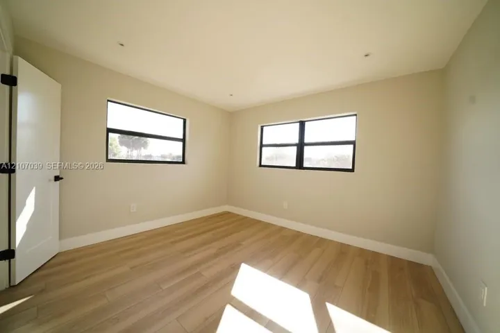 Neutral interior space featuring wood-finish flooring, dual windows with dark frames, recessed lighting, and a shaker-style interior door with matte black hardware