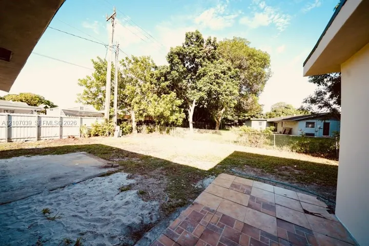 Rear yard featuring a tiled patio, concrete slab, perimeter fencing, and mature trees